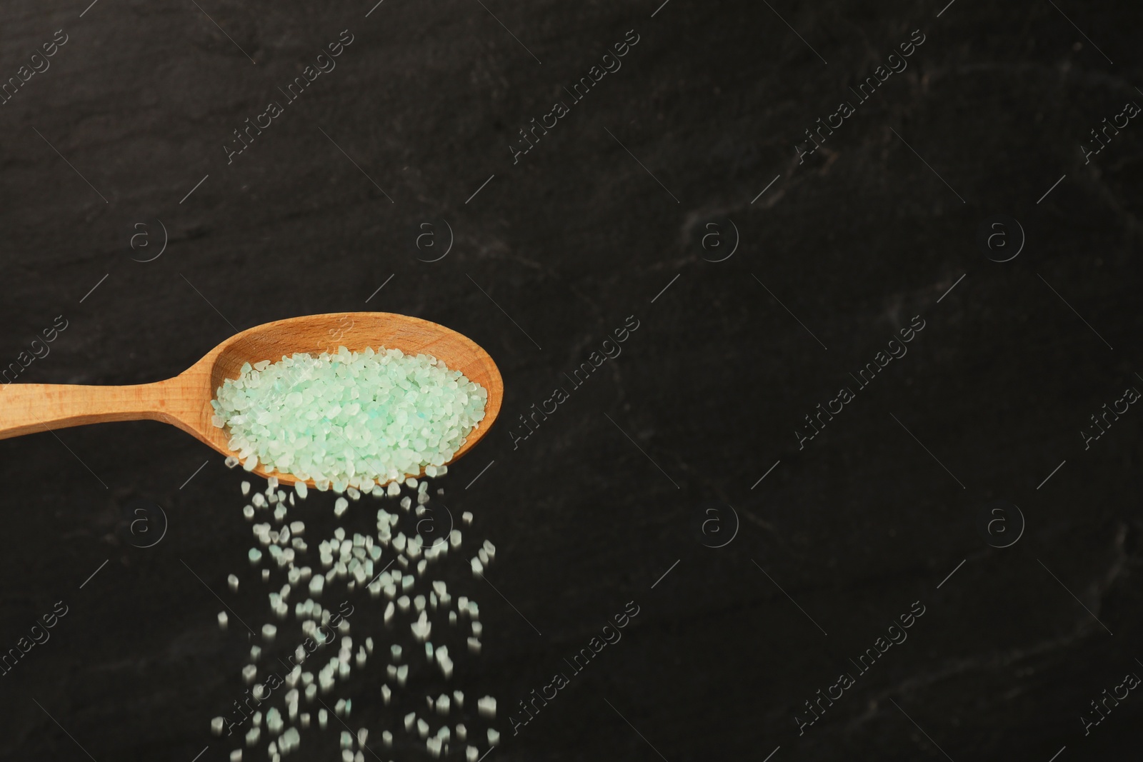 Photo of Pouring turquoise sea salt from wooden spoon against black background. Space for text