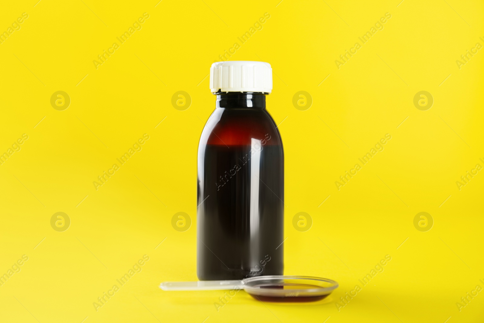 Photo of Bottle of cough syrup and dosing spoon on yellow background