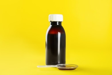 Photo of Bottle of cough syrup and dosing spoon on yellow background