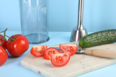 Photo of Hand blender kit, fresh vegetables and knife on light blue background