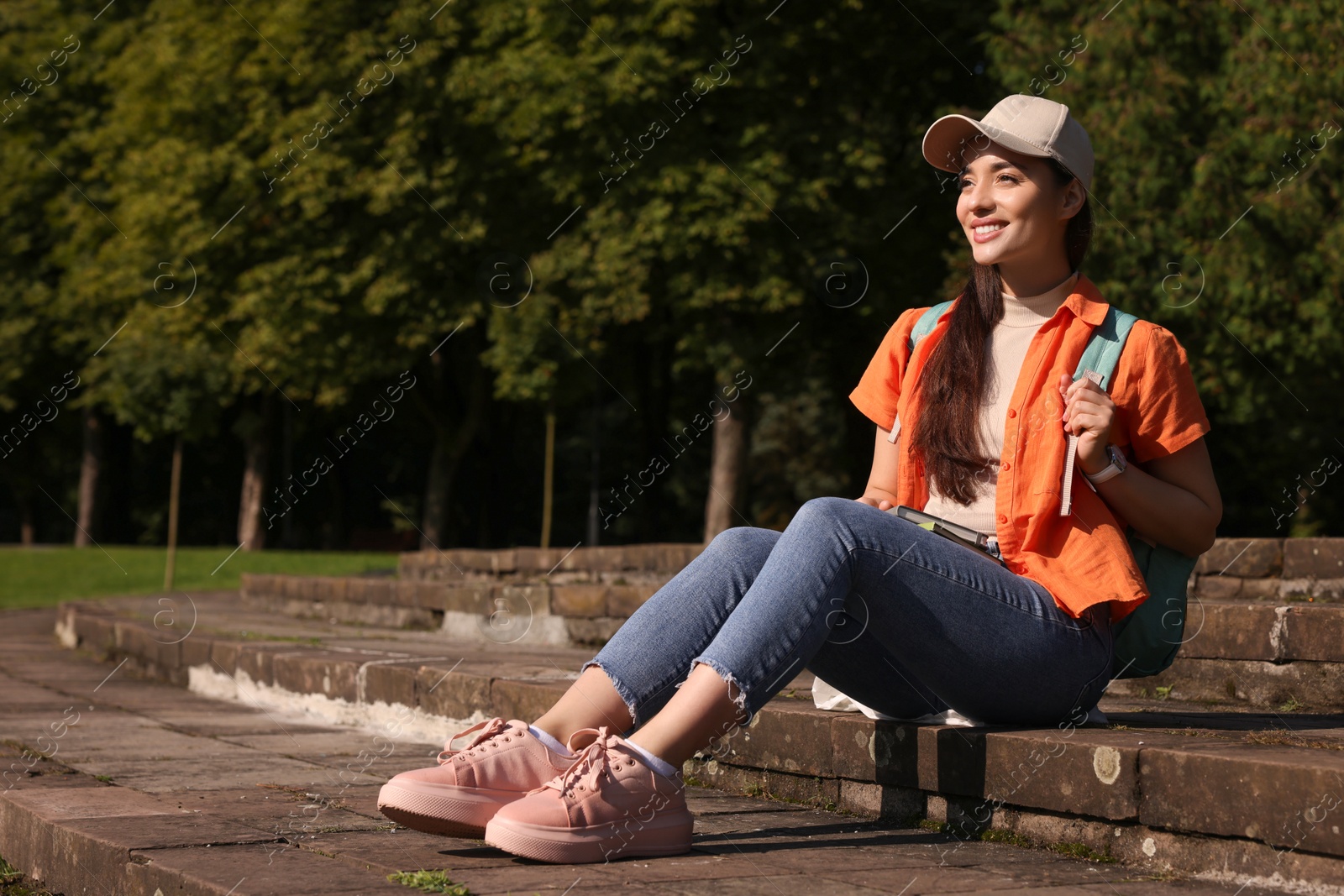 Photo of Happy young student with notebooks on steps in park, space for text