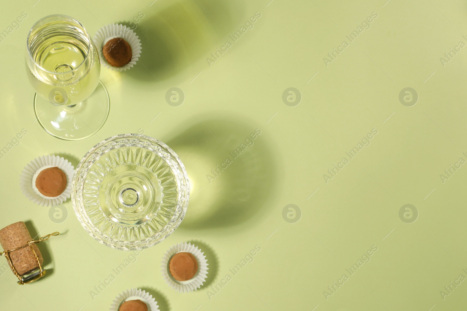 Photo of Glasses of delicious sparkling wine and chocolate truffles on light yellow background, above view. Space for text