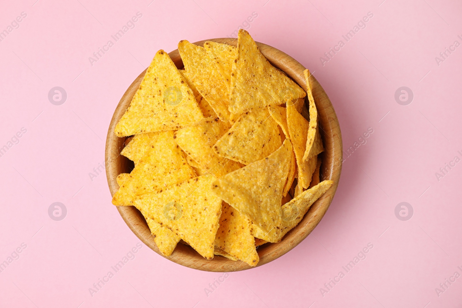 Photo of Wooden bowl with tasty Mexican nachos chips on pink background, top view
