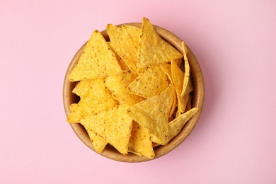Wooden bowl with tasty Mexican nachos chips on pink background, top view