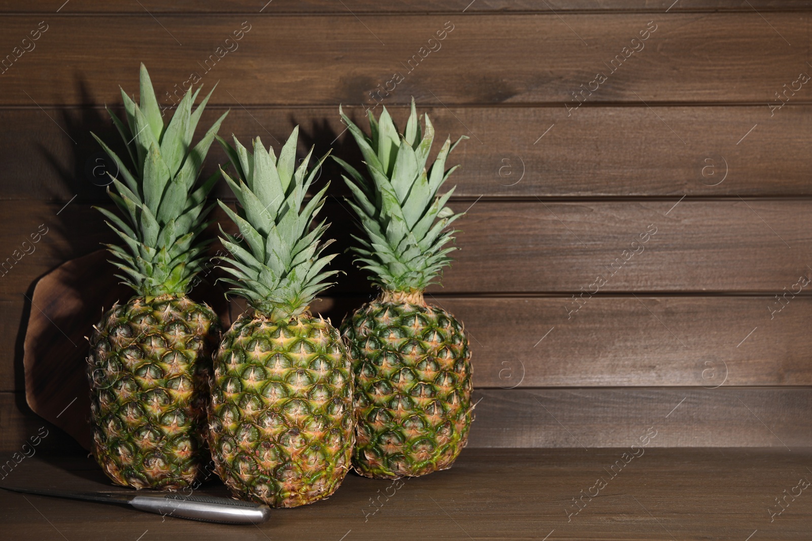 Photo of Whole ripe pineapples and knife on wooden table. Space for text