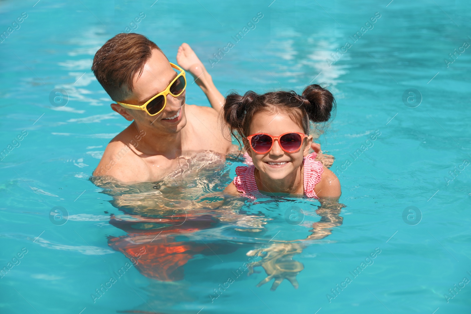 Photo of Young man teaching his daughter to swim in pool
