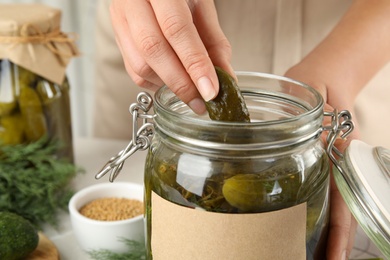 Woman taking pickled cucumber from jar at table, closeup view