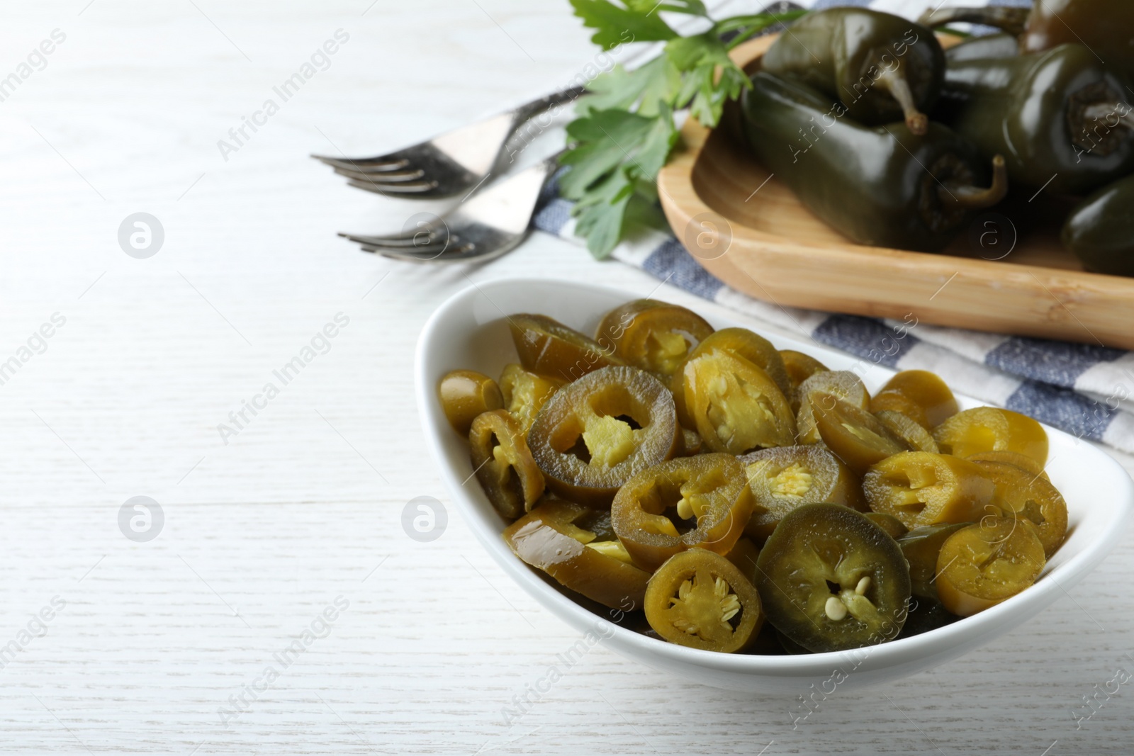 Photo of Bowl with slices of pickled green jalapeno peppers on white wooden table, space for text