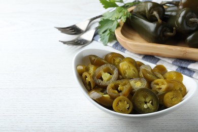 Photo of Bowl with slices of pickled green jalapeno peppers on white wooden table, space for text