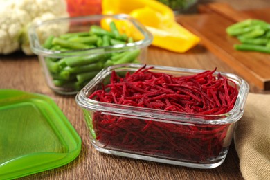 Photo of Containers with cut beetroot and fresh products on wooden table, closeup. Food storage
