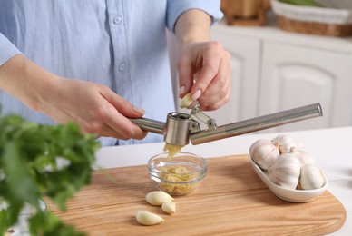 Photo of Woman squeezing garlic with press at wooden table in kitchen, closeup