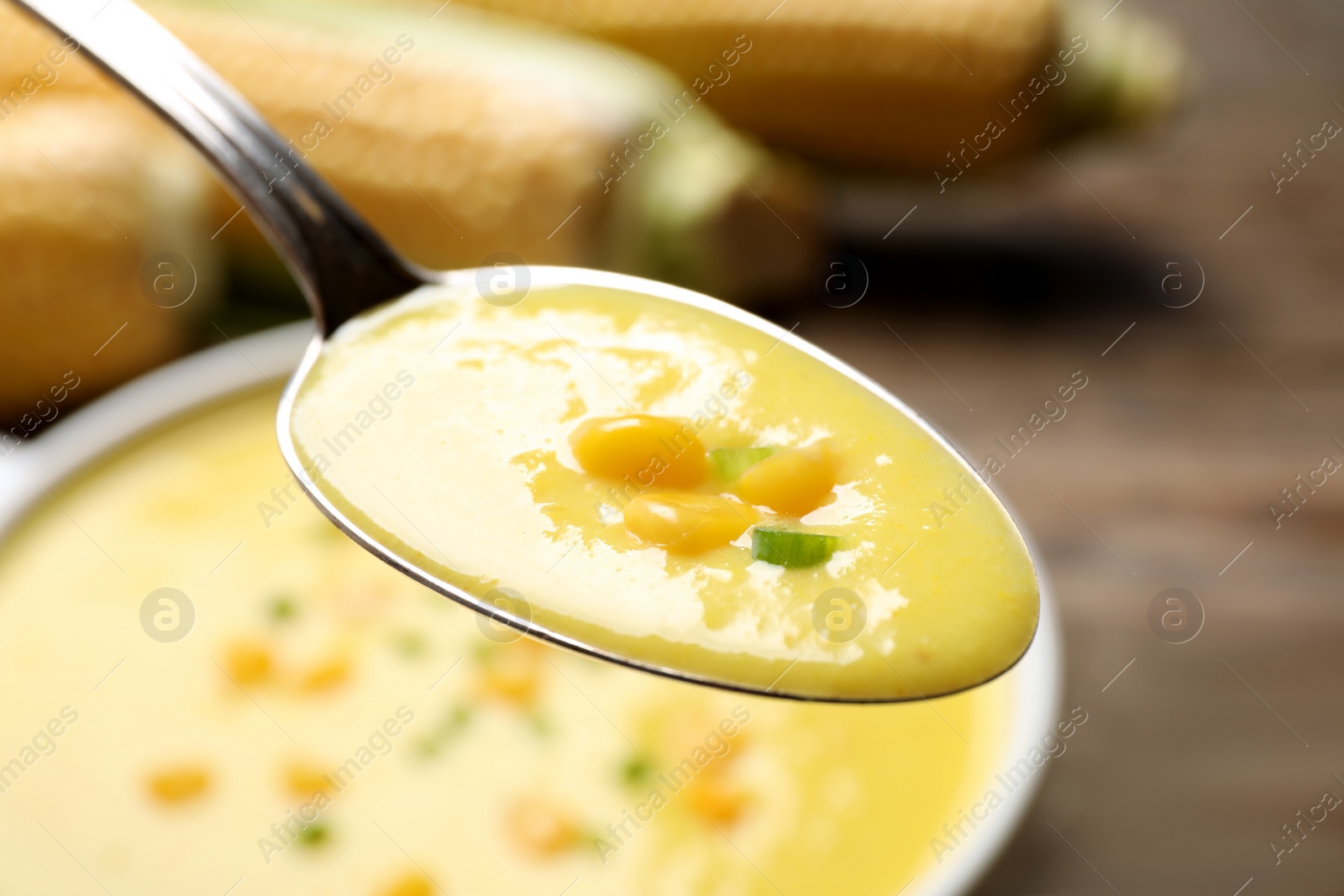 Photo of Spoon of delicious corn soup over full bowl, closeup