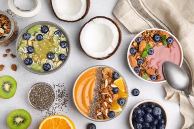 Bowls with different delicious smoothies and fresh ingredients on white table, flat lay