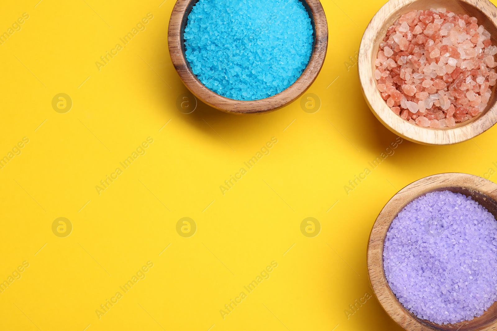 Photo of Different sea salt in bowls on yellow background, flat lay. Space for text