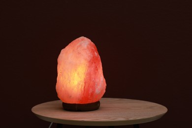 Himalayan salt lamp on wooden table near brown wall, space for text
