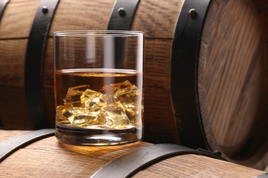 Whiskey with ice cubes in glass on wooden barrel, closeup. Space for text