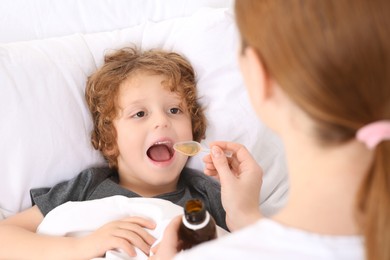 Photo of Mother giving cough syrup to her son on bed