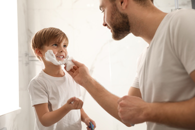 Dad applying shaving foam onto son's face in bathroom