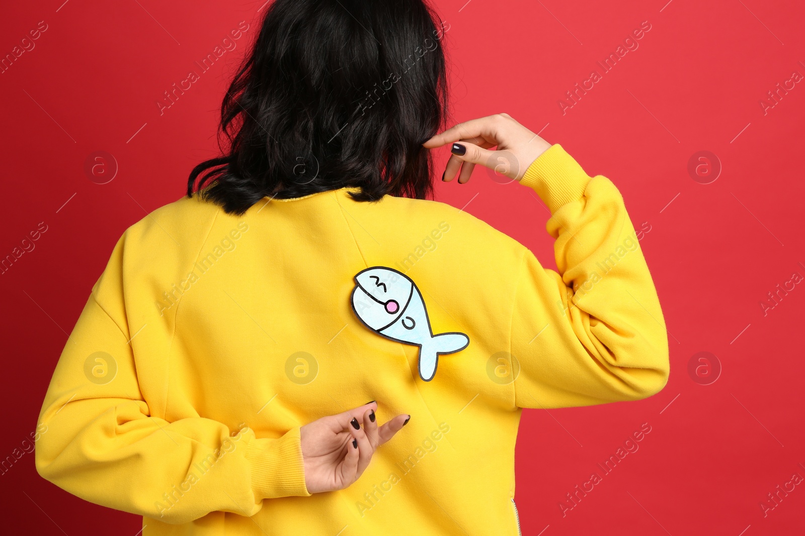 Photo of Woman with paper fish on back against red background. April fool's day