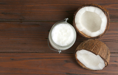 Photo of Halves of ripe coconut and organic oil on wooden table, flat lay with space for text. Healthy cooking