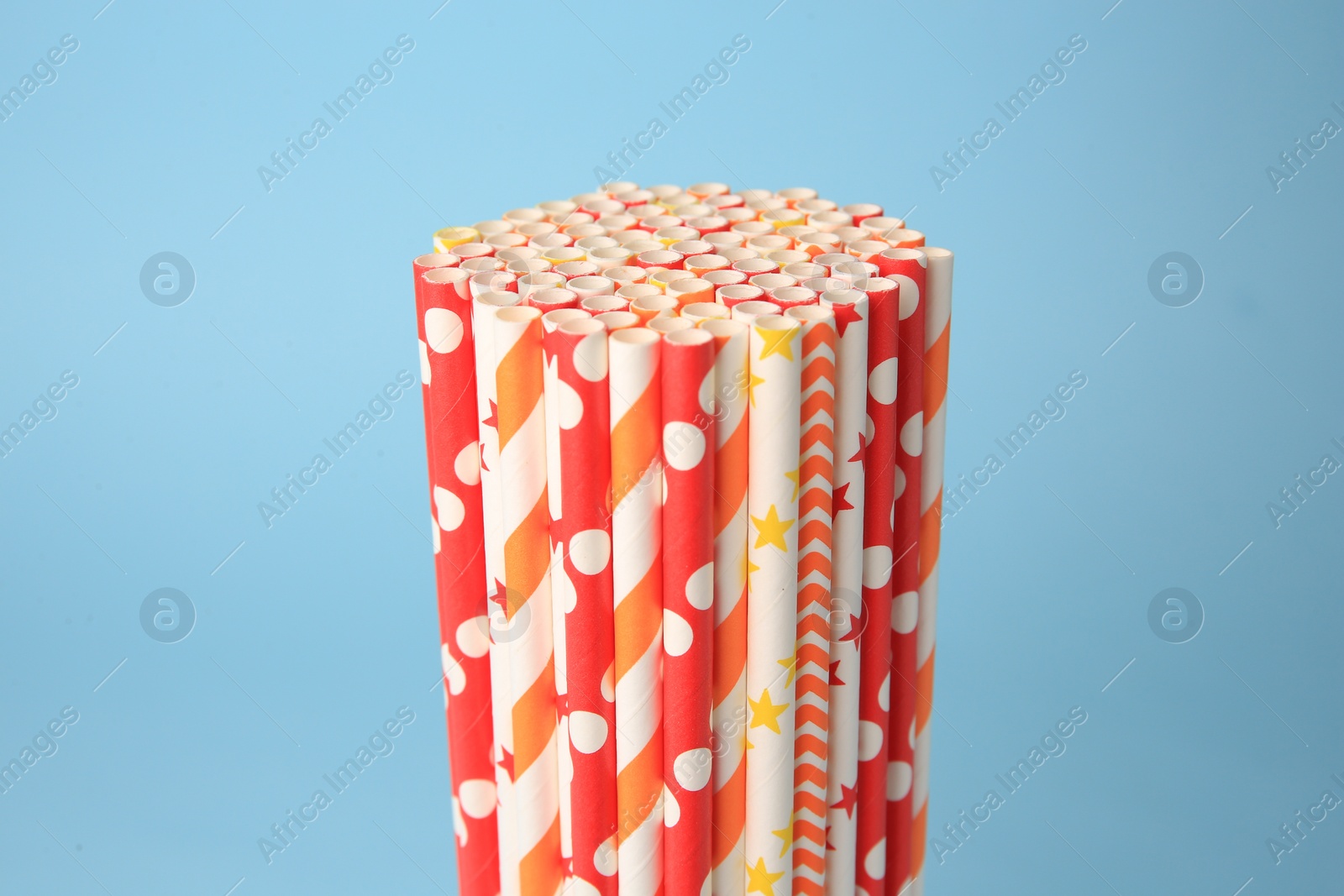 Photo of Colorful paper drinking straws on light blue background, closeup