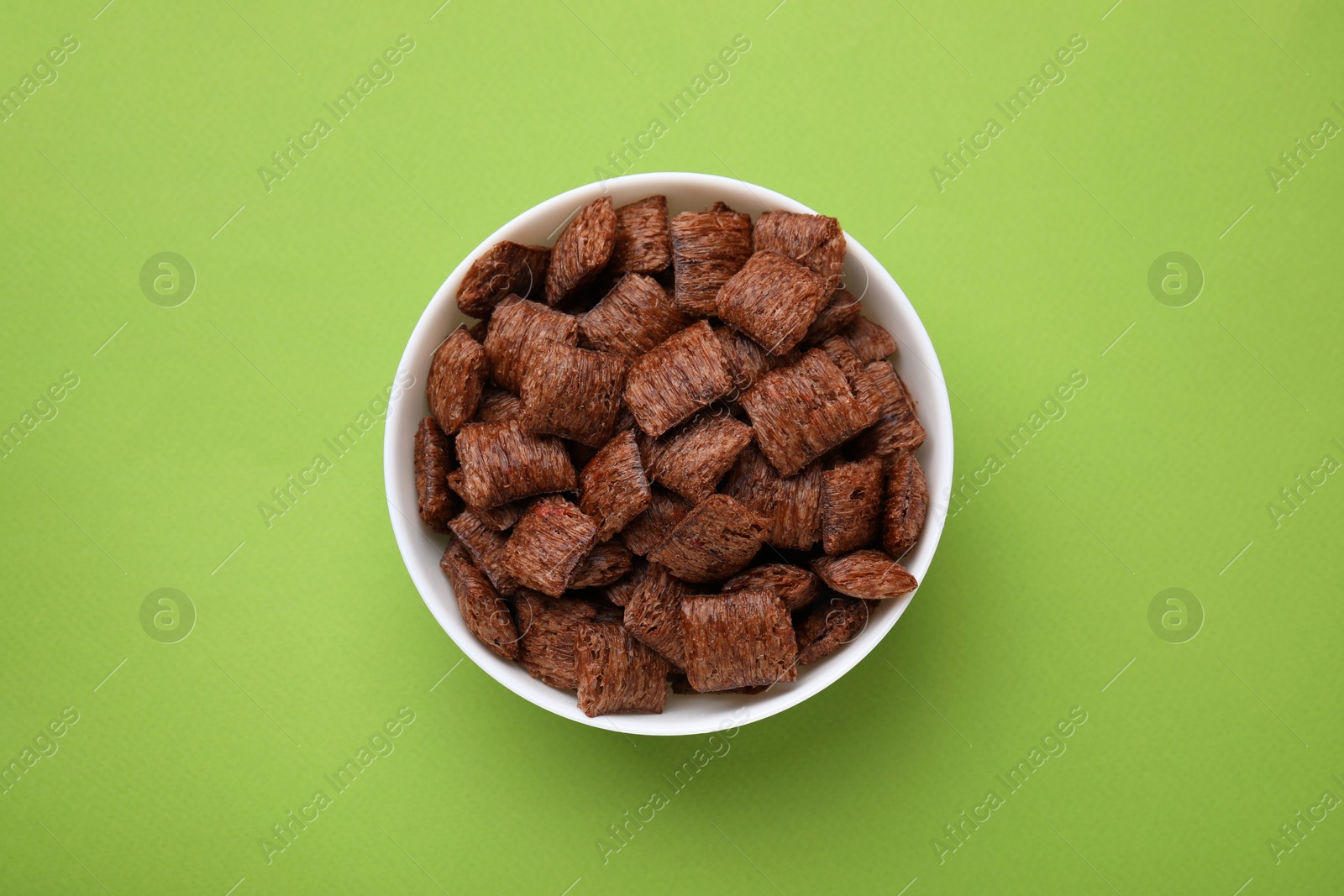 Photo of Chocolate cereal pads in bowl on green table, top view