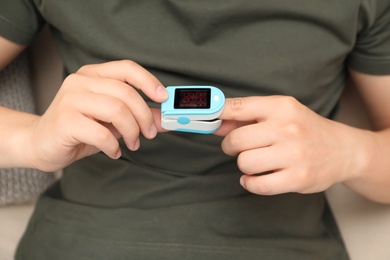 Photo of Young man checking pulse with blood pressure monitor on finger, closeup