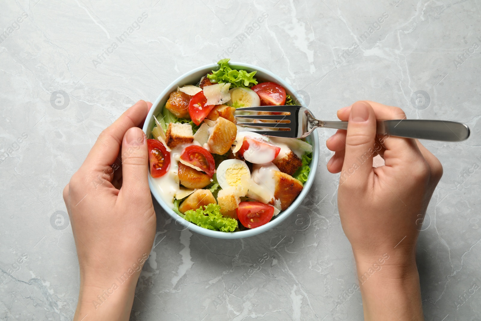 Photo of Woman with bowl of delicious Caesar salad at grey marble table, top view