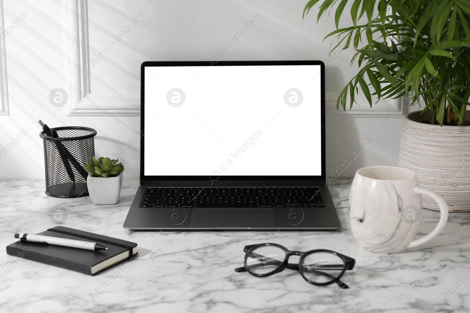 Photo of Office workplace with computer, glasses, cup and stationery on marble table near white wall