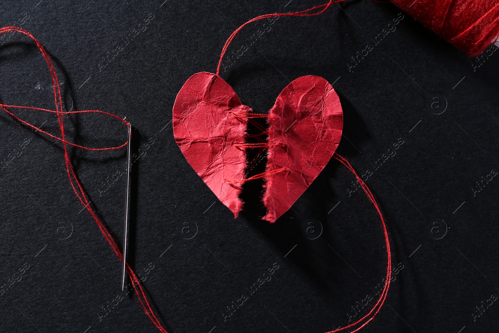 Photo of Halves of torn paper heart connected by thread on black background, flat lay. Relationship problem concept