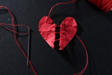 Photo of Halves of torn paper heart connected by thread on black background, flat lay. Relationship problem concept