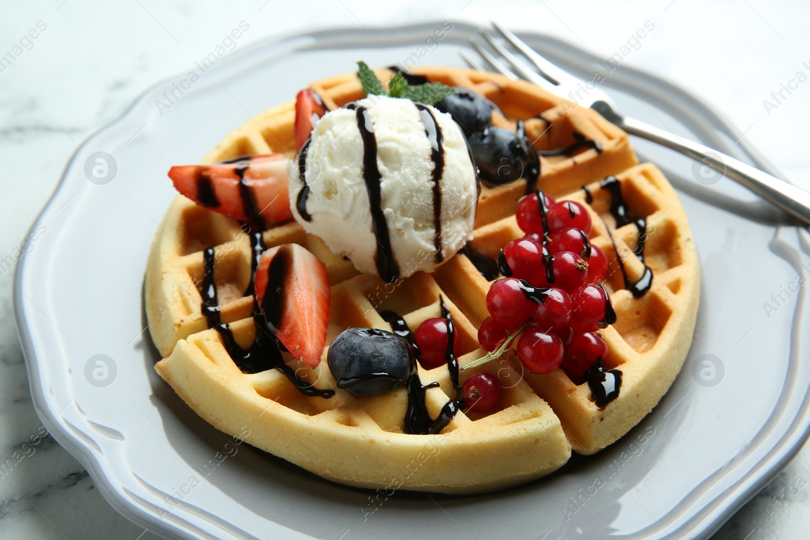 Photo of Delicious Belgian waffles with ice cream, berries and chocolate sauce on light marble table, closeup