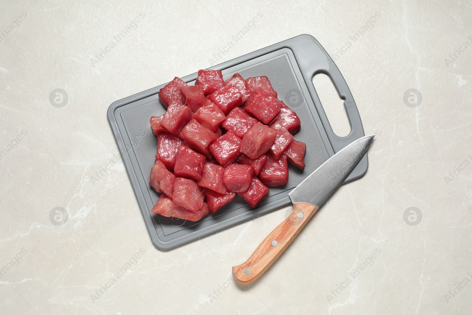 Photo of Cooking delicious goulash. Raw beef meat and knife on light grey table, top view