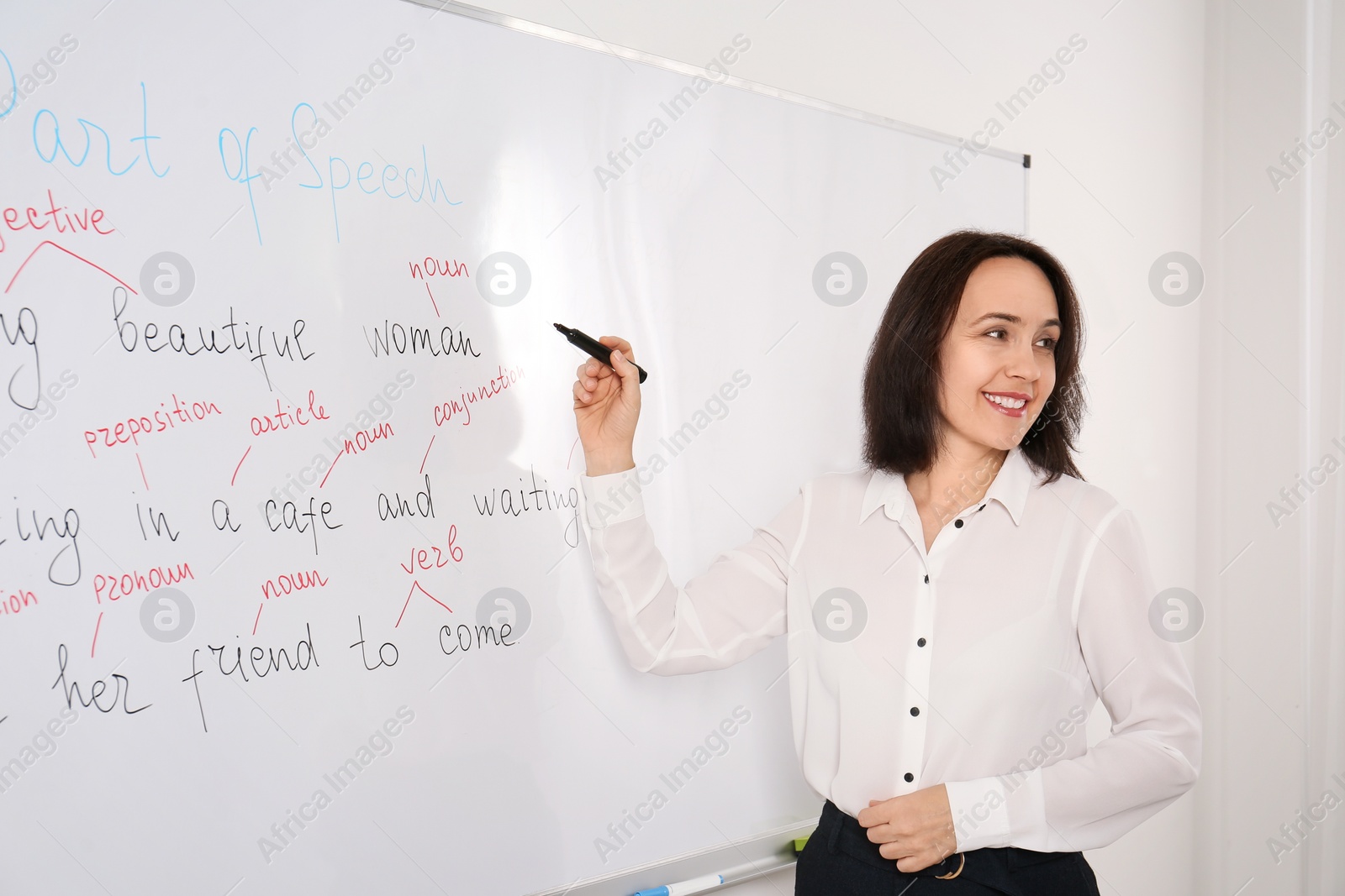 Photo of English teacher giving lesson near whiteboard in classroom