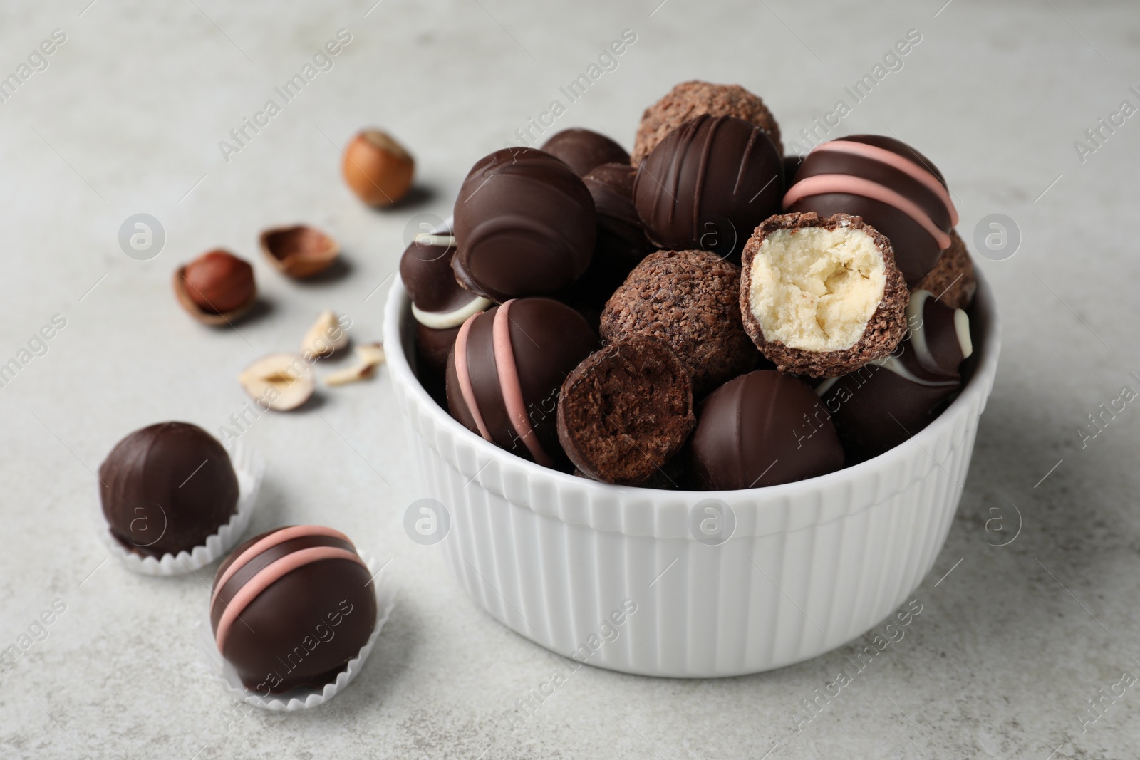 Photo of Different delicious chocolate truffles in bowl on light grey table