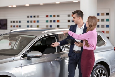 Photo of Young salesman working with client in car dealership