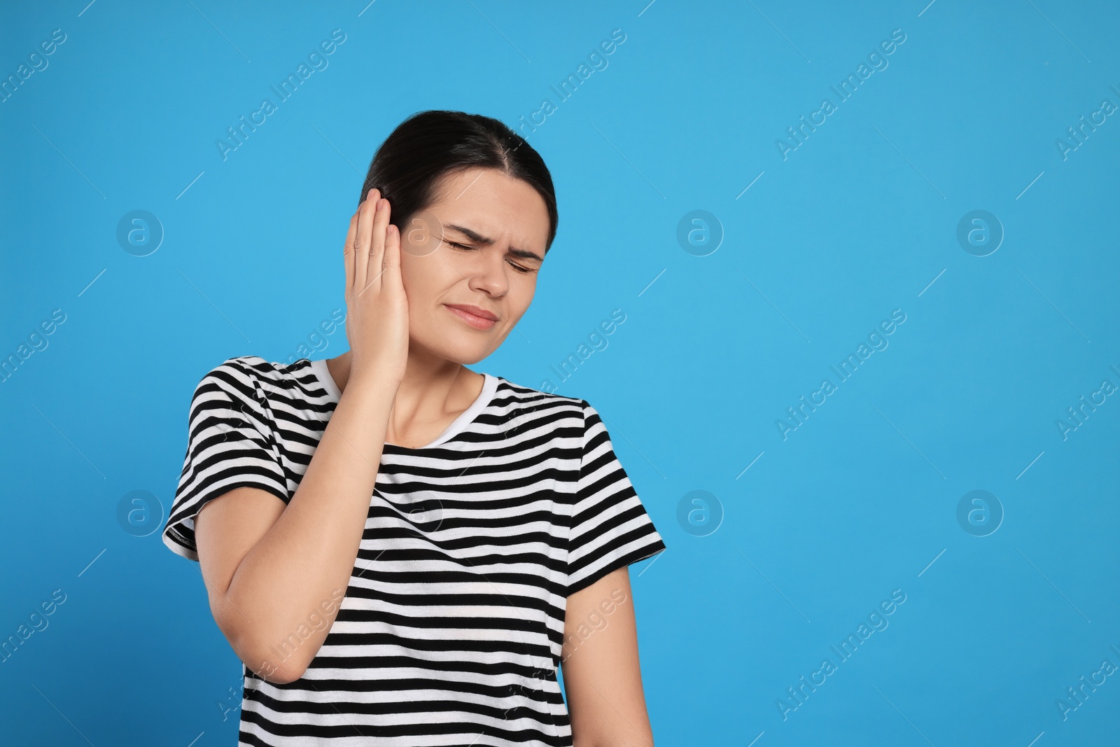 Photo of Young woman suffering from ear pain on light blue background, space for text