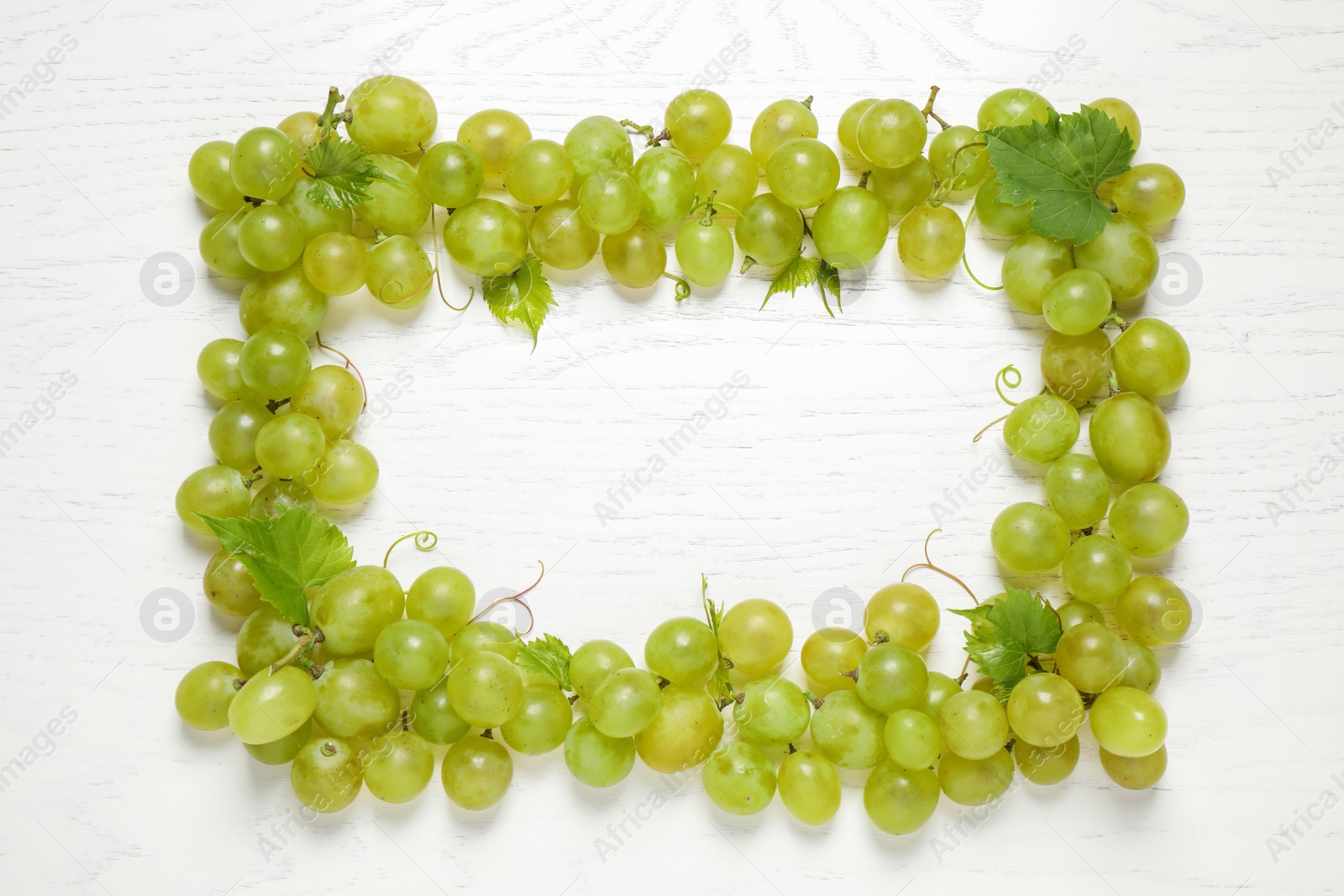 Photo of Frame made with fresh ripe juicy grapes on white wooden table, space for text