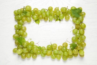 Frame made with fresh ripe juicy grapes on white wooden table, space for text