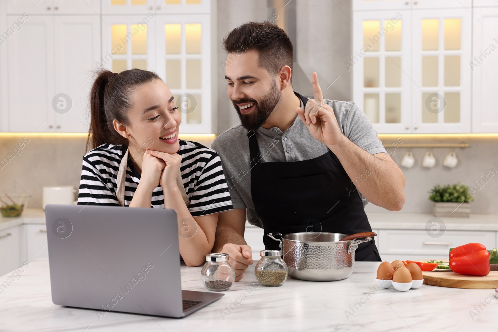 Photo of Happy lovely couple using laptop while cooking in kitchen