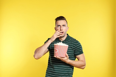 Emotional man with popcorn during cinema show on color background