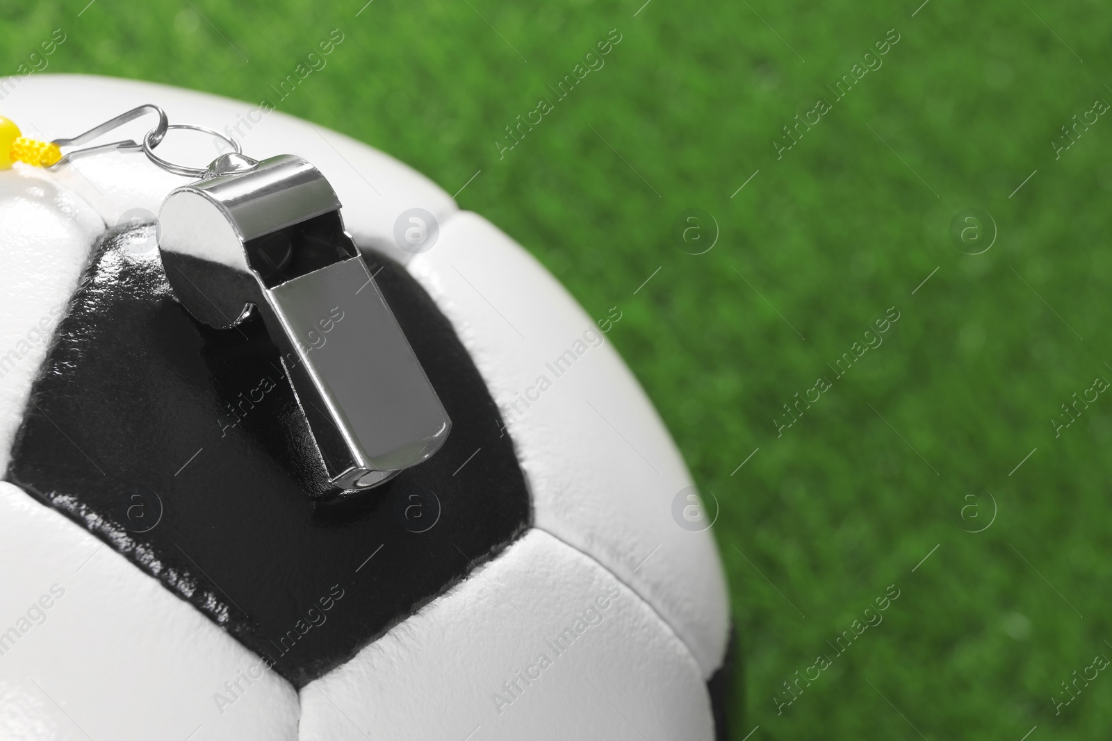 Photo of Football referee equipment. Soccer ball and metal whistle on green grass, closeup with space for text