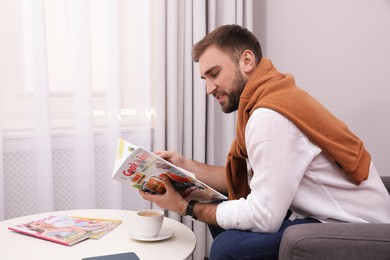 Photo of Handsome man reading magazine near window at home