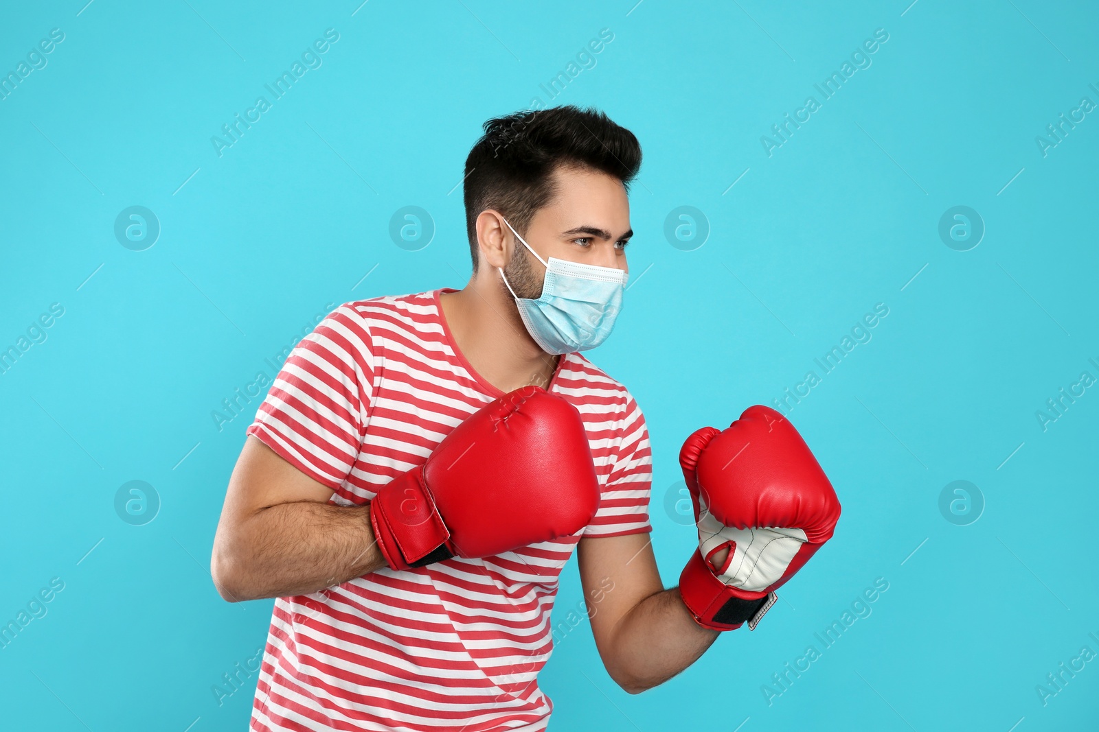 Photo of Man with protective mask and boxing gloves on light blue background. Strong immunity concept