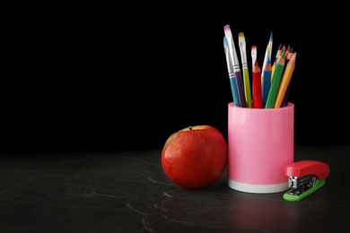 Photo of Different school stationery and apple on stone table near blackboard, space for text. Back to school