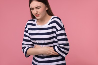 Photo of Young woman suffering from stomach pain on pink background