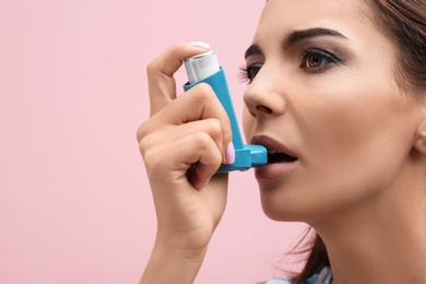 Young woman using asthma inhaler on color background, closeup