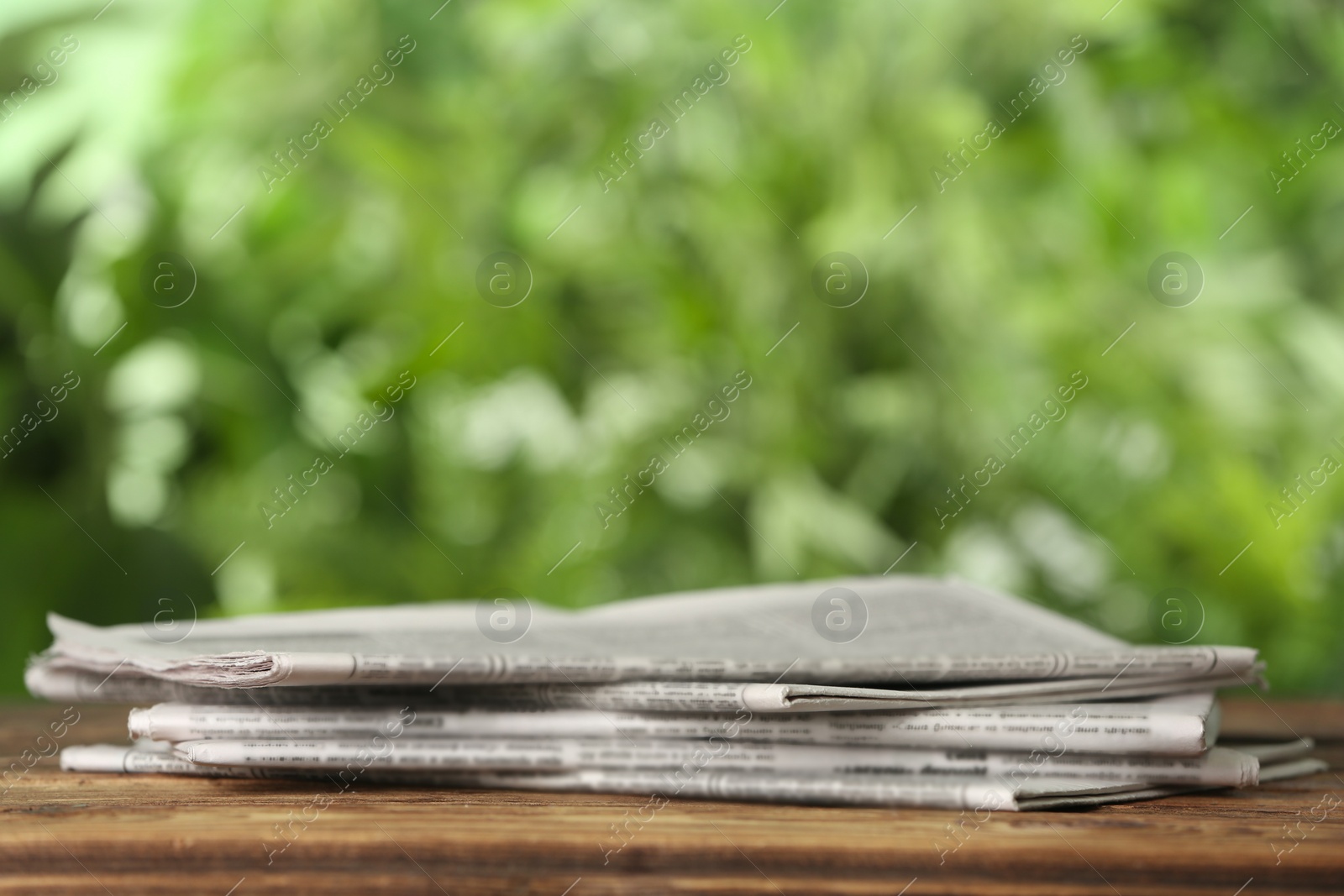 Photo of Newspapers on wooden table against blurred green background, space for text. Journalist's work