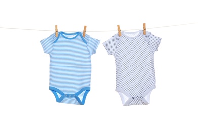 Colorful baby onesies hanging on clothes line against white background. Laundry day