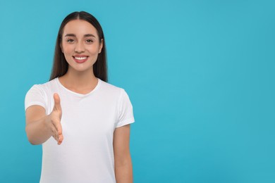 Photo of Happy young woman welcoming and offering handshake on light blue background, space for text